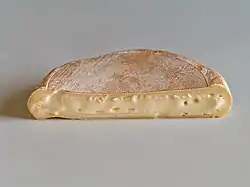 Half-circle of soft tan cheese, cut side forward, on white table