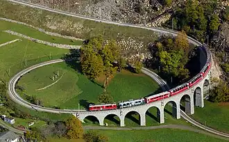A train moving atop a stone bridge in an attractive valley