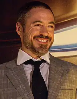 Downey smiling warmly, dressed in a plaid suit jacket with a white shirt and a black tie.