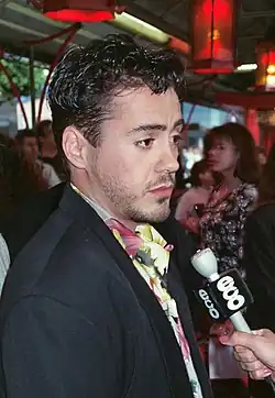 A 25-year-old Downey dressed in a dark blazer and colorful shirt, being interviewed with a microphone