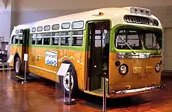An old bus displayed at a museum. The destination sign says Cleveland Ave, and the number 1857 is printed between the headlights. The bus is painted in vibrant shades of white, green, and yellow.