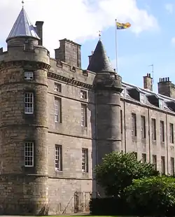 The Royal Standard of the United Kingdom, (Scottish variant), featuring the Royal Banner of Scotland in the first and fourth quarters, flying over Holyrood Palace, Edinburgh.