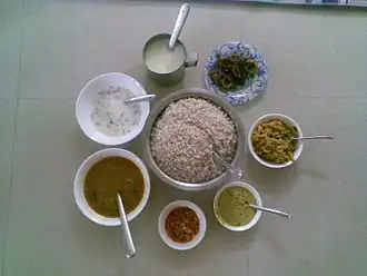 Sadhya items ready to be served. Clockwise from top: paayasam or pradhaman, bitter gourd thoran, aviyal, kaalan, lime pickle, sambar, and buttermilk with boiled rice in center