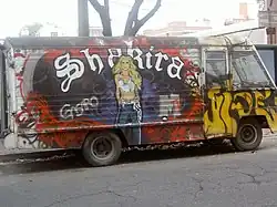A portrait of a woman dressed in a white crop top and blue pants is painted on a colourful van. The word "Shakira" is written in white behind her.
