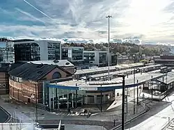 Sheffield bus and coach Interchange is in the foreground, in the bottom left corner is the main entrance. In the centre are long bus stands that form the interchange. Above that is the Digital Campus built upon an unused part of the interchange. In the top left corner is the 1960s Park Hill flats and to the right is Sheffield station.