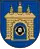 A coat of arms depicting a grey castle with three towers topped by crosses with a human head on the front door all on a blue background