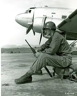 A man sits on equipment with an aircraft in the background.