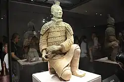 A kneeling Terracotta Army archer wearing with a shirt, an armoured jacket, a short skirt with underneath trousers, and a shallow-mouth shoes, Qin dynasty