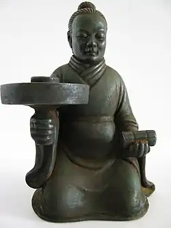A candle stick holder depicting a man in a robe with a youren opening, Southern dynasty (420-589 AD).