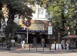 A brown-bricked building with a rectangular, dark blue sign reading "ST. JOHN'S WOOD STATION" in white letters all under a light blue sky