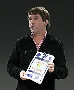 Stephen Hillenburg stands holding a book looking off to his right