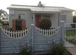 A small, detached one-story house. The walls are a pale colour, and the roof is made from corrugated iron.
