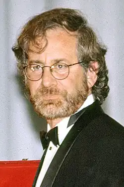 Portrait of a man with long wavy hair and a short beard wearing wire-frame glasses