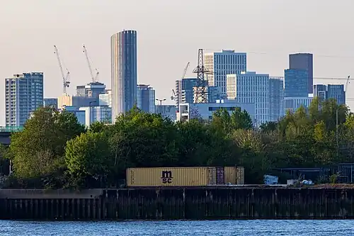 The emerging cluster in Stratford in April 2023 as viewed from Greenwich Peninsula. Stratford has been undergoing regeneration, associated with the 2012 Summer Olympics, which largely took place in Queen Elizabeth Olympic Park to the west of the cluster. Seen on the left is 150 High Street at a height of 135&nbsp;m. The tallest building in the cluster, Manhattan Loft Gardens at 143&nbsp;m, is seen at the back.