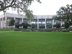 A two-story, white building in the shape of a crescent overlooks flowers and a grassy lawn