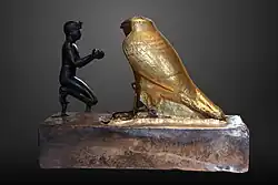 Taharqa offering wine jars to Falcon-god Hemen;[76] 690–664 BC; bronze, greywacke, gold and wood; length: 26&nbsp;cm, height: 19.7&nbsp;cm, width: 10.3&nbsp;cm; Louvre