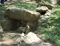 A stone-lined channel set into a grassy embankment. The sides of the channel are formed by upright stones and parts of the channel are covered with capstones.