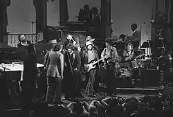 A black and white photo of about a dozen musicians performing on a stage.