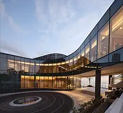 A curved, glass walkway over a pavilion leading to a building