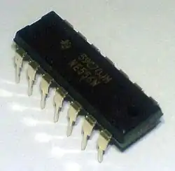 Close up of a small black rectangular microprocessor chips with small gold-colored metallic prongs extending from the side downward. The top middle portion that reads "59C70JN, NE556N".