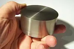 A hand holding a cylinder of reflective silvery metal