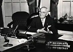Man in suit sitting behind desk with sign that says "The buck stops here"