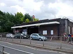 A brown-bricked building with a rectangular, dark blue sign reading "UPNEY STATION" in white letters all under a light blue sky with white clouds