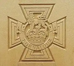 The cross pattée bearing the crown of Saint Edward surmounted by a lion with the inscription FOR VALOUR etched into stone.