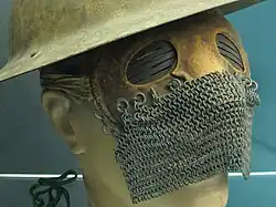a mask with a leather upper with slits on the metal eyepieces, and a chain mail lower, modelled on a dummy head with a metal war helmet