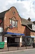 A brown-bricked building with a rectangular, dark blue sign reading "WEST HAMPSTEAD STATION" in white letters all under a blue sky