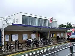 A brown-bricked building with a rectangular, dark blue sign reading "WEST RUISLIP STATION" in white letters all under a light blue sky