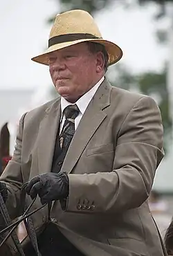 Shatner is on horseback wearing saddle seat attire during a show.
