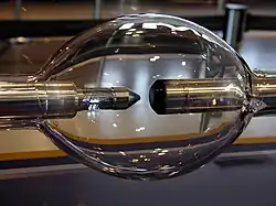 Elongated glass sphere with two metal rod electrodes inside, facing each other. One electrode is blunt and another is sharpened.