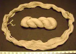 A hank of wool yarn (center) is uncoiled into its basic loop. A tie is visible at the left; after untying, the hank may be wound into a ball or balls suitable for knitting. Knitting from a normal hank directly is likely to tangle the yarn, producing snarls.