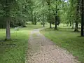 A gravel path runs across grass dotted with trees