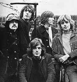A black-and-white photo of the five band members standing in front of a brick wall in 1968