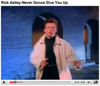 Video screenshot with the title "Rick Astley - Never Gonna Give You Up". It shows the singer dancing, wearing a trenchcoat over a turtleneck.