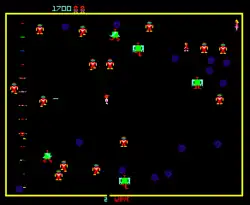 A horizontal rectangular video game screenshot that is a digital representation of a confined black space with a red and white character in the center. The character shoots a robot while surrounded by a large group red and yellow robots with several larger green robots among them. A female human is in the top right corner while the number "1700" is at the top left corner.