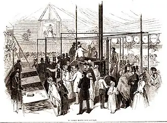 Interior of temporary building with large boiler in them middle and stores and serving stations at each side. The space is full of the great and good in smart clothes for the official opening ceremony