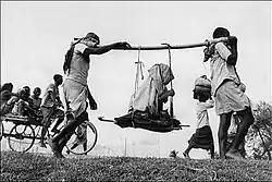 Two Muslim men (in a rural refugee train headed towards Pakistan) carrying an old woman in a makeshift doli or palanquin, 1947.