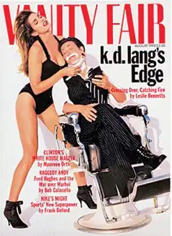 Cover of Vanity Fair magazine from August 1993 showing k.d. lang reclining in a barber chair with eyes closed and holding a compact mirror. She has shaving foam on her chin and is wearing an open-collar white shirt, black and white striped tie, dark color pinstripe vest and cuffed pants, and black lace boots. Supermodel Cindy Crawford is holding a straight razor to lang's chin while lang's head rests on her breast. Crawford is wearing a one-piece black bathing suit and high heel black boots, with head thrown back as her long hair cascades down her back.
